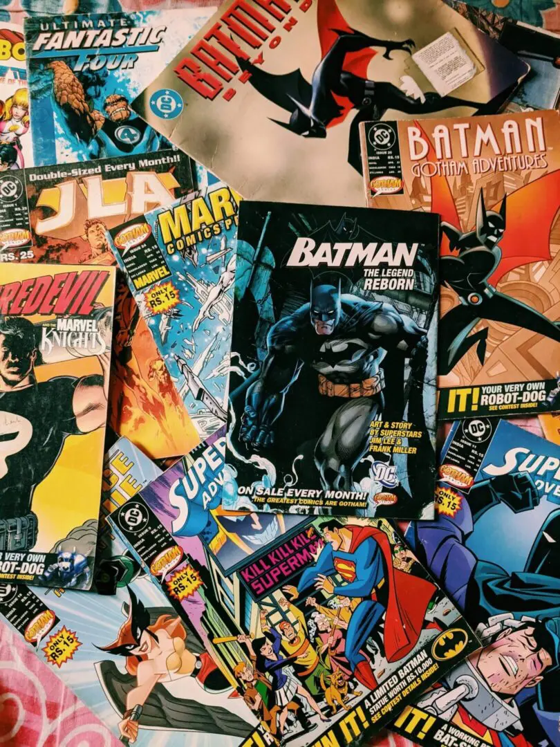 A variety of comic books featuring characters like Batman, Superman, and members of the Justice League, scattered on a surface.