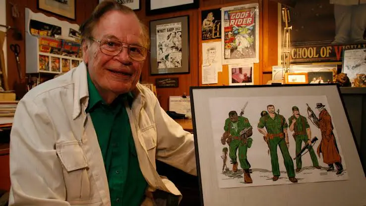 Elderly man smiling beside framed artwork of soldiers.